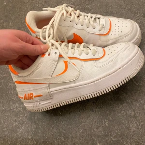 Nike Air Force i vitt och orange -  Nike Air Force sneakers. De har klassisk snörning och är . Skorna är i bra skick med lite slitage på sulan men knappt, har använd 3-4 ggr. Observera:   Har inte torkat rent dem eller tvättat de på bilden