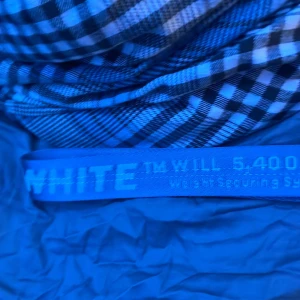 Blått bälte från Off-White - Säljer ett coolt blått bälte från Off-White med texten 'WEIGHT SECURING SYSTEM' och '5,400 lbs'. Bältet har en unik design med en robust spänne och är perfekt för att ge din outfit en edgy touch. Den är äkta köpte den från farfetch jag tror typ 3000kr det var länge sen jag köpte den pris kan diskuteras.