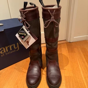Bruna stövlar från Dubarry - Snygga och funktionella bruna stövlar från Dubarry med Gore-Tex. Perfekta för utomhusaktiviteter med snörning upptill och robust design. Tillverkade i skinn och mocka för hållbarhet och stil. Storlek 39 använd ett fåtal gånger. 
