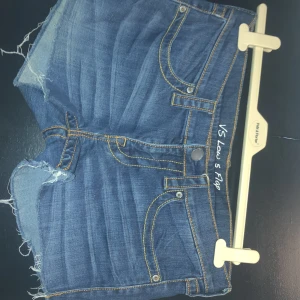 Blå jeansshorts från London Jean - Snygga blå jeansshorts från London Jean med fransiga kanter och klassisk femficksdesign. Perfekta för en avslappnad stil. De har en knapp och dragkedja framtill. Storlek 8 motsvarar ungefär 38.