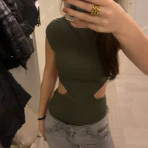 Body  - En populär och snygg olivgrön body med tight passform och unika utskärningar i midjan. Perfekt för en trendig look. Prislappen finns kvar! ALDRIG ANVÄND!(Bara testad) först till kvarn!!