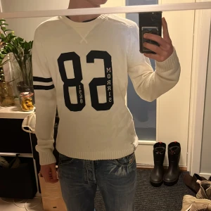 Vit tröja från Morris - Säljer en stilren vit tröja från Morris med trycket '68' och svarta ränder på ärmen. Tröjan har ribbstickade muddar och en klassisk passform. Perfekt för en avslappnad och sportig look.