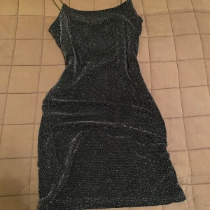 Svart glittrig klänning från H&M - Snygg svart klänning från H&M med glittriga detaljer. Den har smala axelband och en figurnära passform som ger en elegant look. Perfekt för festliga tillfällen.