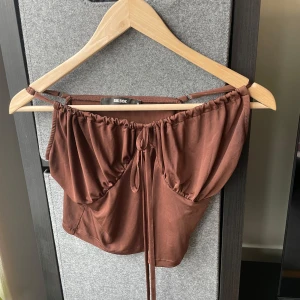 Topp från Bik Bok - Snygg brun topp från Bik Bok med knytband framtill. Perfekt för en trendig look. Toppen har en avslappnad passform och är tillverkad i ett mjukt material.