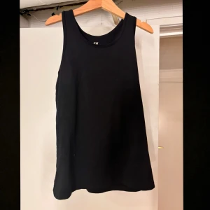 Svart linnetopp från H&M - Snygg och enkel svart linnetopp från H&M. Perfekt för varma dagar eller som lager under andra plagg. Den har en klassisk rund halsringning och ärmlös design. Man kan träna i den också 