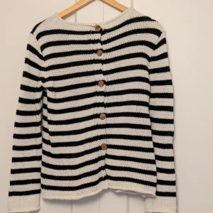 Randig stickad tröja från Salt - Säljer en snygg randig stickad tröja från Salt i svart och vit. Tröjan har långa ärmar och knappar längs ryggen för en unik look. Perfekt för kyligare dagar.