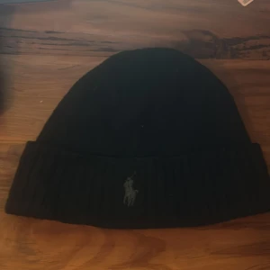 Svart mössa från Polo Ralph Lauren - Snygg svart mössa från Polo Ralph Lauren med broderad logotyp. Tillverkad i mjuk ull för extra värme och komfort. Perfekt för kyliga dagar. Skriv vid frågor!!