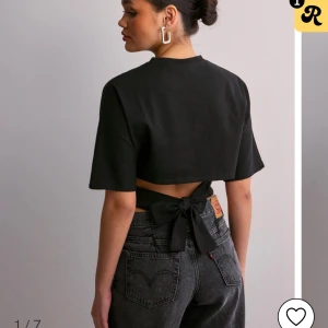 Svart croppad topp med knyt - Trendig svart croppad topp med knyt i ryggen från Nelly. Perfekt för en stilren look. Den är i bra skick🩷