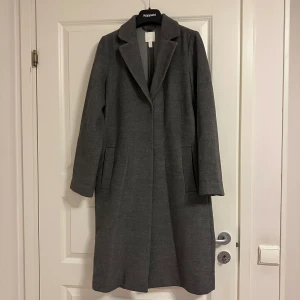 Grå kappa från H&M - Snygg mörkgrå kappa från H&M i en klassisk design. Perfekt för höst och vinter.