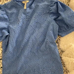 Blå spetsblus från Object - Säljer en söt blå spetsblus från Object i storlek XS. Blusen har korta ärmar och ett vackert spetsmönster som ger en romantisk känsla. Perfekt för vår och sommar! Aldrig använd 