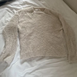 Beige fluffig tröja från H&M - Mysig beige tröja från H&M i fluffigt material. Perfekt för kyliga dagar med sin mjuka och varma känsla. Tröjan har långa ärmar och en enkel design som gör den lätt att matcha med olika outfits.