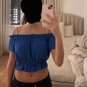 Blå offshoulder topp - Snygg blå offshoulder topp med elastisk midja och volangdetaljer. Perfekt för sommarens varma dagar. Toppen har korta ärmar och en croppad passform.