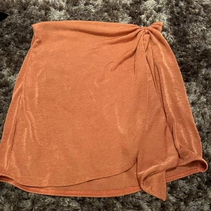 Brun omlottkjol - Snygg brun omlottkjol med en elegant knytning i sidan. Kjolen har en mjuk och flödande design som ger en avslappnad look. Perfekt för att skapa en stilren outfit.