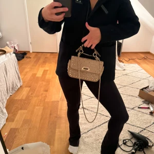 Mörkblå duffel Zara storlek 164 - Snygg beige axelväska med guldkedja och nitar. Perfekt för att ge din outfit en edgy touch. Väskan har en praktisk dragkedja och en stilren design.