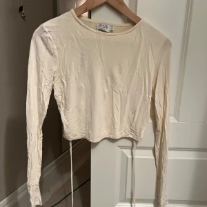 Beige långärmad topp med öppen rygg - Snygg beige långärmad topp från NAKD med öppen rygg och knytband. Perfekt för en trendig look. Toppen är croppad och har en stilren design.