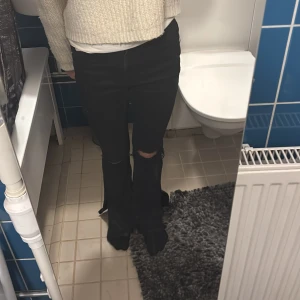 Svarta bootcut jeans med slitningar - Snygga svarta bootcut jeans med slitningar på knäna. Perfekta för en avslappnad stil. De har en dragkedja och knappar framtill.