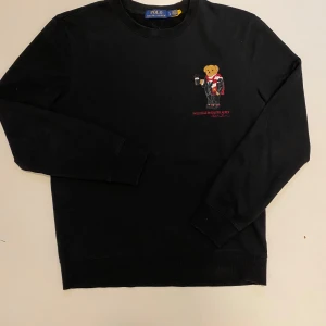 Ralph Lauren polo bear tröja - Säljer en svart tröja från Ralph Lauren med det ikoniska Polo Bear-motivet broderat på bröstet. Tröjan har långa ärmar och en klassisk rund halsringning. Perfekt för en stilren och avslappnad look. Den är i väldigt bra skick utan hål, slitningar eller likande, skriv vid minsta fråga eller fundering💯👍