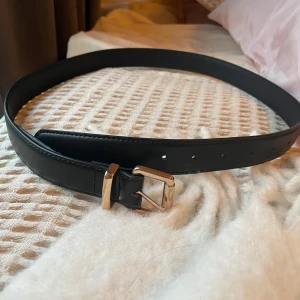 Svart bälte från Gina Tricot - Snyggt svart bälte från Gina Tricot med ett stilrent spänne. Perfekt för att ge en elegant touch till din outfit. Tillverkat i skinnimitation och passar bra till både jeans och klänningar. Helt nytt och aldrig använt❤️