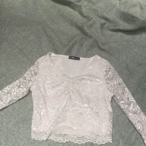 Vit spetsblus från Fab Sister - Elegant vit spetsblus från Fab Sister med v-ringning och långa ärmar. Blusen har ett vackert spetsmönster och passar bra till både jeans och kjol. Tröjan är ärvd men passar inte på mig och har därför aldrig använt den. 