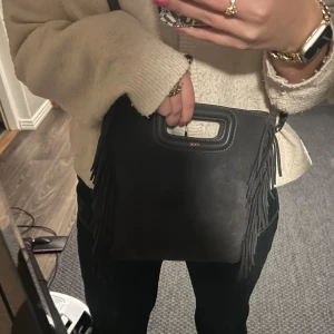 Maje väska mörkgrå  - Snygg grå axelväska i mocka från Maje med coola fransdetaljer. Väskan har ett praktiskt handtag och en justerbar axelrem. Magnet öppning, så smidigt och rymmer så mycket. Jättesnygg grå färg 