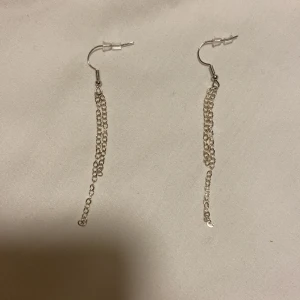 Silvriga örhängen med kedjor  - Eleganta och stilrena silvriga örhängen med hängande kedjor. Perfekta för att ge en extra touch till din outfit. Lätta och bekväma att bära hela dagen.