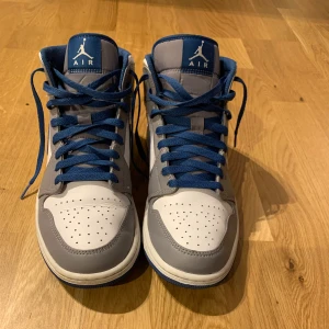 jordan 1 - Snygga Nike Air Jordan sneakers i en stilren kombination av blått, grått och vitt. Skorna har klassisk snörning och en ikonisk design med Air Jordan-loggan på sidan. Dom är i väldigt bra skick och har använts endast ett fåtal gånger. Storleken är 44 men passar 43