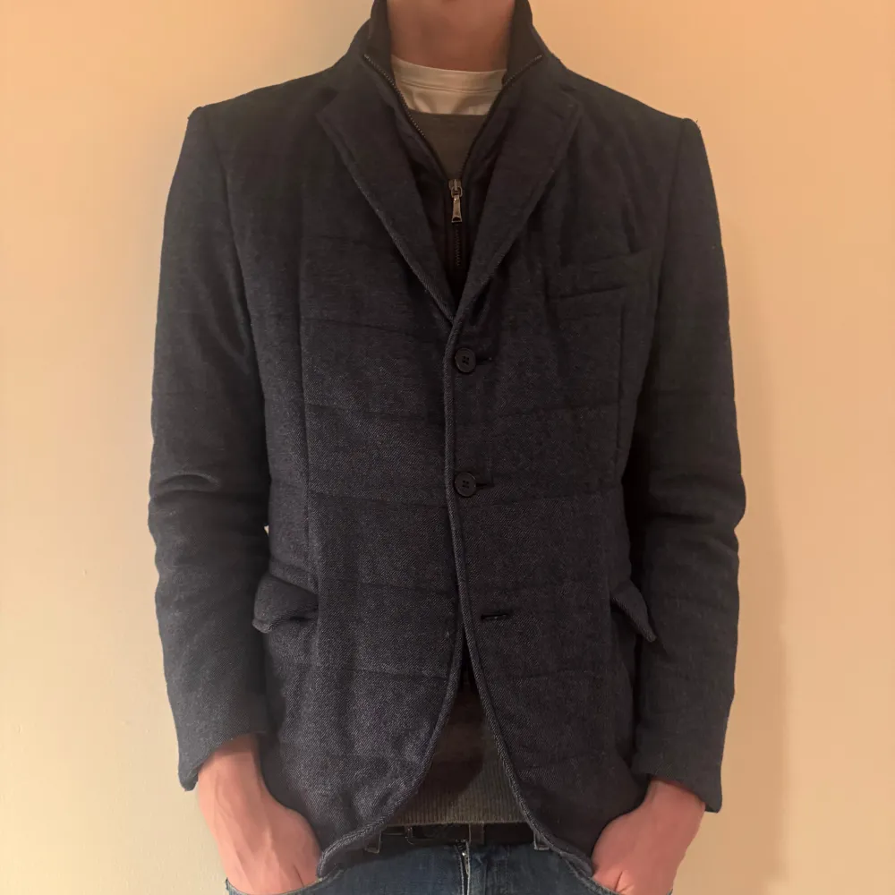 Snygg mörkblå kavaj från Boggi Milano med quiltad design och knappar framtill. Perfekt för en stilren look. Kavajen har långa ärmar och en klassisk krage. Funkar bäst på hösten och våren men funkar även i en varmare vinter. En knapp saknas men går att sy på och hänger med kavajen på köp. Förutom det är kavajen i topp skick. Modellen är drygt 190 cm.. Takit.
