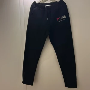 Svarta mjukisbyxor från Trapstar - Snygga svarta mjukisbyxor från Trapstar med broderad logga i rött, svart och vitt. Byxorna har snörning i midjan och är perfekta för en avslappnad stil.