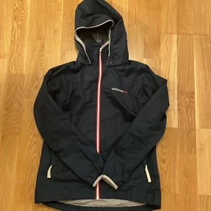 Dark blue  regnjacka från Didriksons - Säljer en dark blue  regnjacka från Didriksons med huva och dragkedja. Jackan är 100% vattentät och tillverkad i polyester med polyamidfoder. Perfekt för regniga dagar.