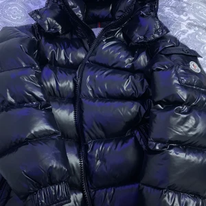 Moncler Maya  - Snygg svart dunjacka från Moncler med glansig finish och dragkedja. Perfekt för kyliga dagar. Storlek 2 vilket är S/M EU storlek 