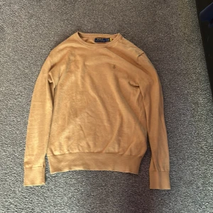 Beige tröja från Polo Ralph Lauren - Säljer en stilren beige tröja från Polo Ralph Lauren. Tröjan har långa ärmar och en klassisk rund halsringning. Perfekt för en avslappnad och elegant look.