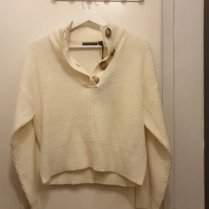 Vit stickad tröja från Brave Soul - Säljer en stilren vit stickad tröja från Brave Soul. Tröjan har en hög krage med stora knappar framtill och långa ärmar. Perfekt för kyliga dagar! Helt ny med lapp på.