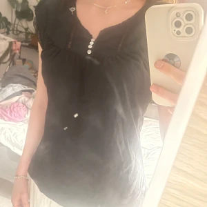 Svart blus med spetsdetaljer - Snygg svart blus med spetsdetaljer vid ärmarna och knappar framtill. Perfekt för en stilren look. Blusen har en lös passform och är ärmlös, vilket gör den bekväm och luftig. Storlek M💕