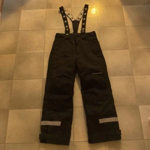 Svarta byxor med hängslen från Cross Sportswear - Säljer ett par svarta byxor med justerbara hängslen från Cross Sportswear. Byxorna har reflexdetaljer vid benen och är perfekta för utomhusaktiviteter. 