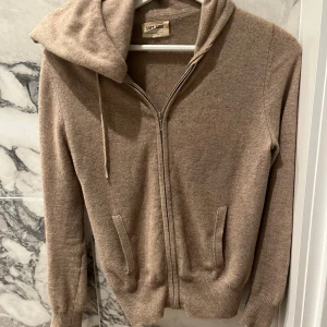Soft goat zip huddie  - Säljer denna beige bruna koftan från soft goat i 100 procent cashmere. Tröjan har två defekter på baksidan av armarna (de som syns på de två sista bilderna) men resten av tröjan är i mycket gott skick. Tröjan går fortfarande att använda med en jacka över eller med uppdragna armar🫶
