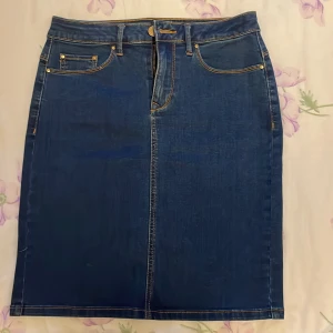 Blå jeanskjol från Vila - Snygg blå jeanskjol från Vila med klassisk femficksdesign och kontrastsömmar. Kjolen har en bekväm passform och är perfekt för en avslappnad stil. Den har en knapp- och dragkedjestängning framtill.