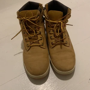 Bruna boots med snörning - Säljer ett par bruna boots från Timberland med snörning och vadderad krage. Modellen är lite sportigare än den traditionella, lite som en sneaker. Perfekta för höst och vinter med en robust design och slitstark sula.