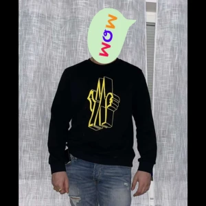 Svart sweatshirt med gult tryck från moncler - Snygg svart sweatshirt med ett iögonfallande gult tryck på framsidan. Tröjan har långa ärmar och en klassisk rund halsringning. Perfekt för en avslappnad stil.