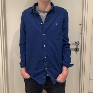 Blå Ralph Lauren skjorta  - Snygg blå skjorta från Ralph Lauren. Felfritt skick förutom att knappen längst där nere saknas. Storlek 18-20 motsvarar en stor S, passar fint på mig cirka 174 men kan även passa någon längre eller lite kortare. Nypris runt 1800 mitt pris 449 (inte hugget i sten) PM vid frågor!🤝