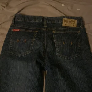 Mörkblå jeans från Mudd - Snygga mörkblå jeans från Mudd med klassisk femficksdesign och dekorativa sömmar på bakfickorna. Jeansen är bootcut och är perfekta för en avslappnad stil. Lite sönder längst ner vid fötterna! 