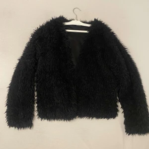 Svart pälsjacka från Gina Tricot - Säljer en snygg svart pälsjacka från Gina Tricot. Jackan har en fluffig textur och är perfekt för att hålla sig varm och stilren. Den är helsvart och har en enkel design utan knappar eller dragkedja. Säljs inte längre