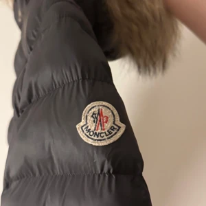 Svart dunjacka från Moncler - Snygg svart dunjacka från Moncler med pälsdetaljer på huvan. 