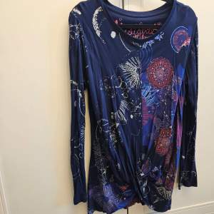Säljer en unik och färgglad långärmad topp från Desigual. Den har ett abstrakt mönster i blått, rött och vitt med en twistdetalj framtill. Perfekt för dig som vill sticka ut med stil!