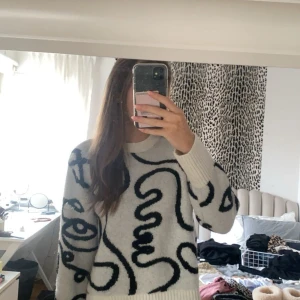 Vit och svart mönstrad tröja - Säljer en superfin vit tröja med svart abstrakt mönster. Den är i storlek M men passar mig med storlek S och har långa ärmar. Perfekt för att hålla sig varm och snygg under kyligare dagar. Tröjan är i nytt skick med prislappen kvar och passar perfekt till både vardag och fest.