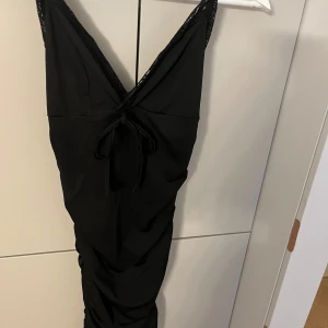 Svart klänning från Shein - Snygg svart klänning från Shein i storlek XS. Den har en v-ringad design med spetsdetaljer och knytning framtill. Perfekt för festliga tillfällen med sin eleganta look. Klänningen är i mycket bra skick och redo för nya äventyr!