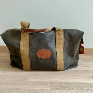 Brun och beige väska från Mulberry - Säljer en snygg och rymlig väska från Mulberry i brunt och beige. Väskan har en robust dragkedja och detaljer i läder. Insidan är fodrad med ett rutigt mönster i mjuka färger. Perfekt för resor eller som en stilren vardagsväska. Kontakta mig för mer info!