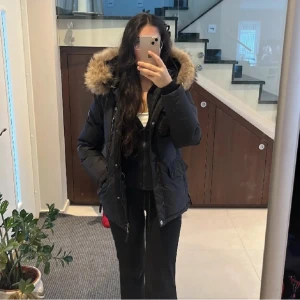 Jacka med päls - Säljer en snygg svart parkajacka med mysig pälsdetalj på huvan. Jackan har långa ärmar och praktiska fickor framtill. Perfekt för kalla vinterdagar och håller dig varm. Säljer då den inte passar mig längre. 