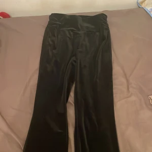 Svarta sammetsbyxor - Säljer ett par svarta byxor i mjukt sammetstyg. De är högmidjade och har en elegant, glansig finish som passar perfekt för festliga tillfällen. Byxorna har en loose passform som ger en bekväm och stilren look. Perfekta för höst och vinter!
