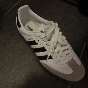 Adidas Samba sneakers - ALDRIG ANVÄNDA!!!! storlek 37 1/3 . Klassiska Adidas Samba sneakers i vitt och svart med snörning. Skorna har en stilren design med de ikoniska tre ränderna på sidan och en gummisula. Perfekta för en sportig och avslappnad stil.  Orginallåda ingår. Köpta för 1345 på zalando. pris kan diskuteras 🩷