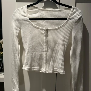 Vit ribbad topp - Säljer en superfin vit ribbad topp med långa ärmar. Den är croppad och har en söt knappdetalj framtill. Perfekt för både vardag och fest! Passar bra till jeans eller kjol. 🖤